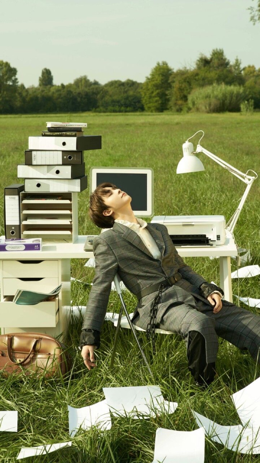 A man reclining in a grass field next to a desk and computer