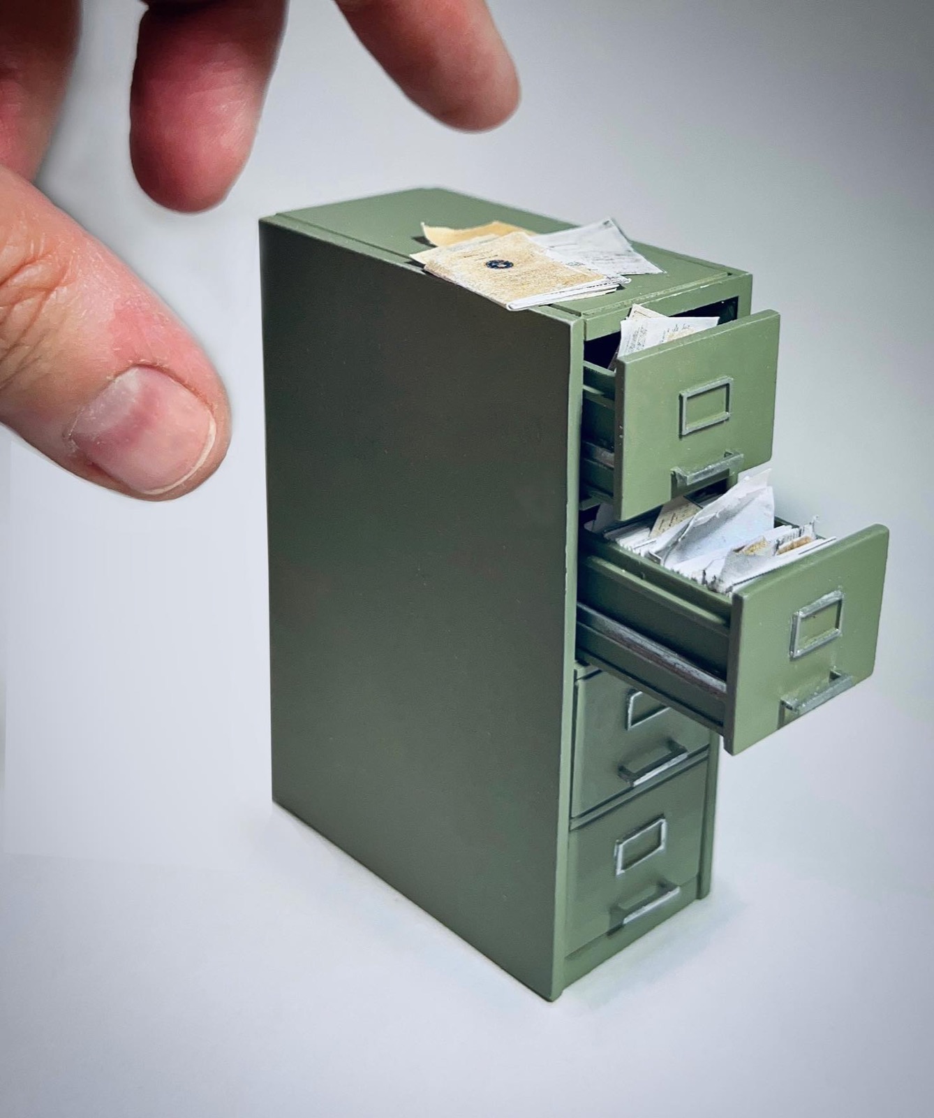 A hand pulling open a green filing cabinet drawer stuffed with papers